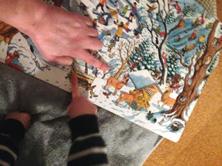 Im Weihnachtswimmelbuch gucken wir uns die Tiere. Dabei zeigt das Kind auf eine Vogelfutterstelle.